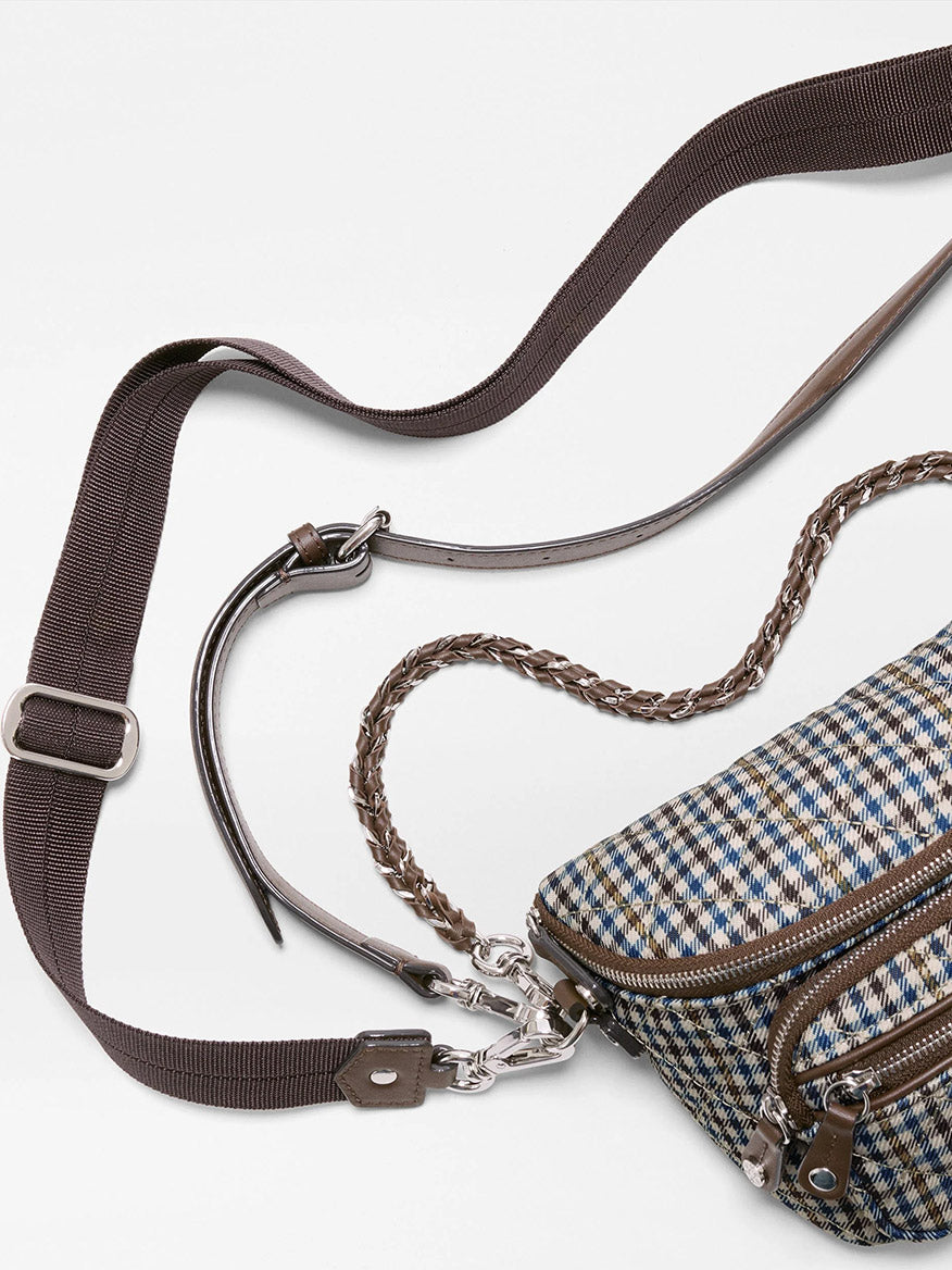 A close-up of the MZ Wallace Micro Sutton Sling in Heritage Check, showcasing its plaid-patterned design with a brown adjustable shoulder strap, braided handle, and silver hardware crafted from premium Italian leather, set against a white background.