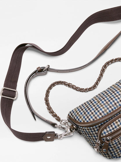 A close-up of the MZ Wallace Micro Sutton Sling in Heritage Check, showcasing its plaid-patterned design with a brown adjustable shoulder strap, braided handle, and silver hardware crafted from premium Italian leather, set against a white background.