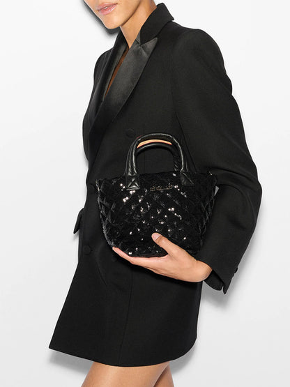 A person in a black blazer is holding the MZ Wallace Micro Metro Tote Deluxe in Black Sequin against a plain white background.