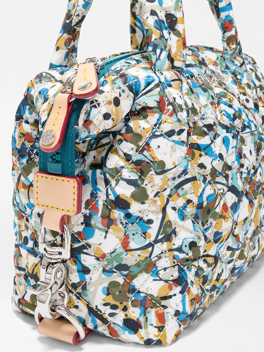Close-up of the MZ Wallace Micro Sutton in Club Paint Oxford, a quilted, foldable crossbody bag featuring an abstract multicolor splatter paint design with beige leather accents and a silver clasp.