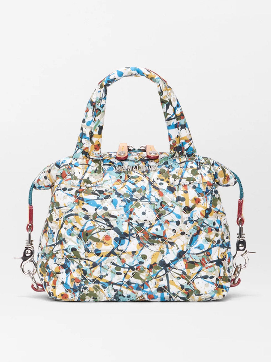 The MZ Wallace Micro Sutton in Club Paint Oxford is a quilted nylon crossbody bag featuring an abstract multicolor paint-splatter pattern, two handles, and detachable red straps. Stylish and foldable, it's shown against a plain background.