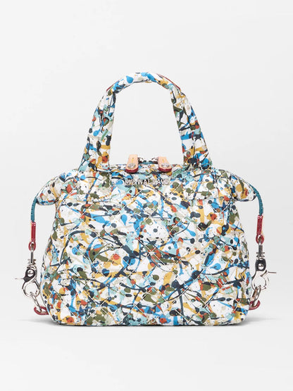 The MZ Wallace Micro Sutton in Club Paint Oxford is a quilted nylon crossbody bag featuring an abstract multicolor paint-splatter pattern, two handles, and detachable red straps. Stylish and foldable, it's shown against a plain background.