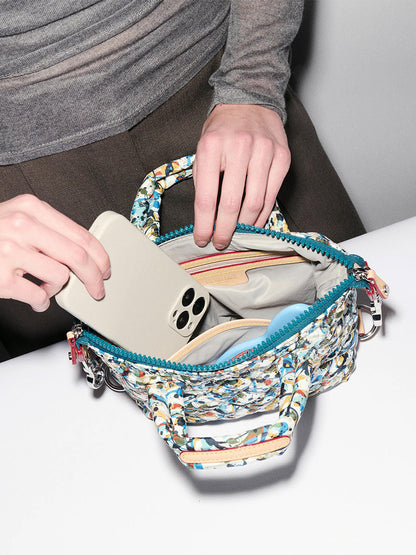 A person places a smartphone into an MZ Wallace Micro Sutton in Club Paint Oxford, its open zipper revealing organized inner compartments.