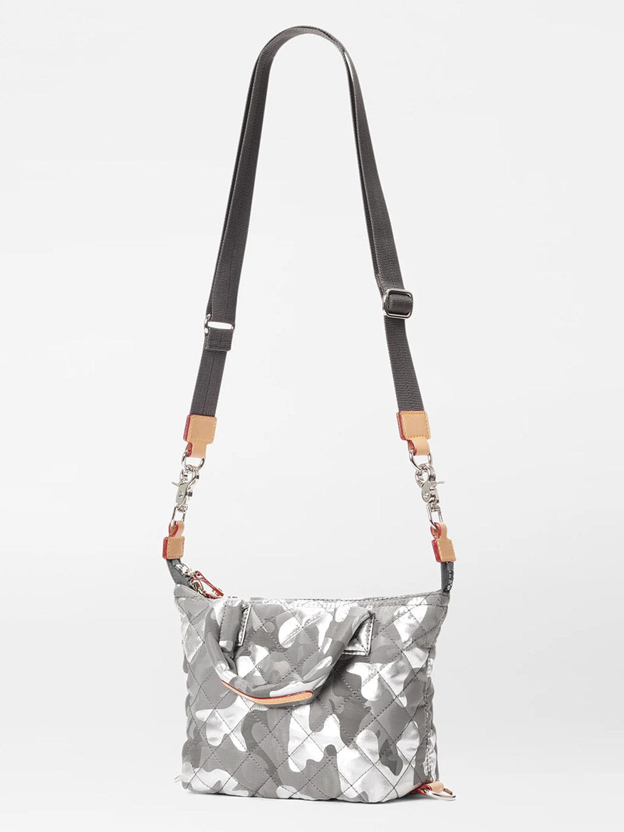 The MZ Wallace Micro Sutton in Silver Metallic Camo Oxford is a small crossbody bag featuring a quilted design, an adjustable strap, and leather accents on the sides, all set against a plain white background. This foldable bag is perfect for any occasion.