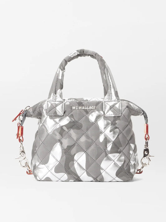 The MZ Wallace Micro Sutton in Silver Metallic Camo Oxford is a small, quilted handbag with short handles, a detachable crossbody strap, and a gray camouflage pattern. Made from recycled oxford material, it features the brand name "MZ WALLACE" on the front.