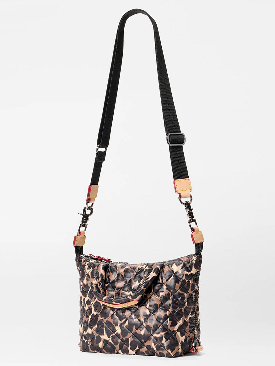 The MZ Wallace Micro Sutton in Leopard Oxford features a black and brown leopard print, adjustable black strap, tan handle, red zippers, and is made from recycled oxford material. Stylishly displayed on a white background.