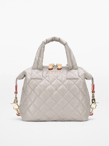 The MZ Wallace Micro Sutton in Sable Pearl Metallic Oxford is a small quilted gray handbag with gold hardware, short handles, and decorative side clasps, shown against a plain light background.