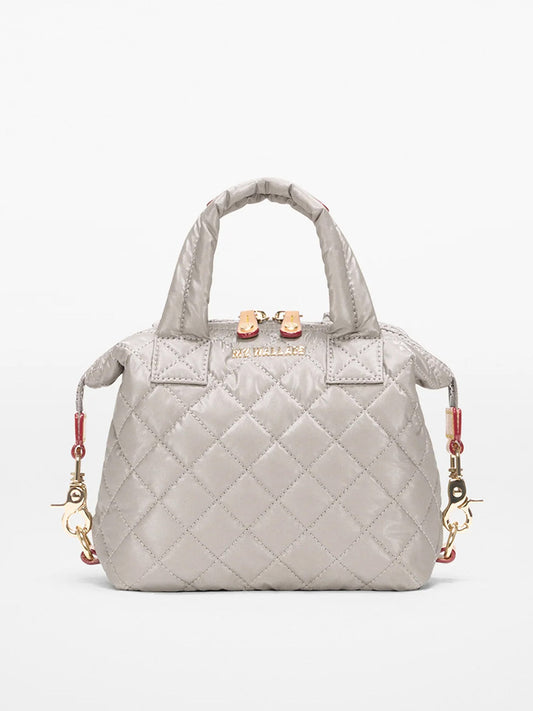 The MZ Wallace Micro Sutton in Sable Pearl Metallic Oxford is a small quilted gray handbag with gold hardware, short handles, and decorative side clasps, shown against a plain light background.