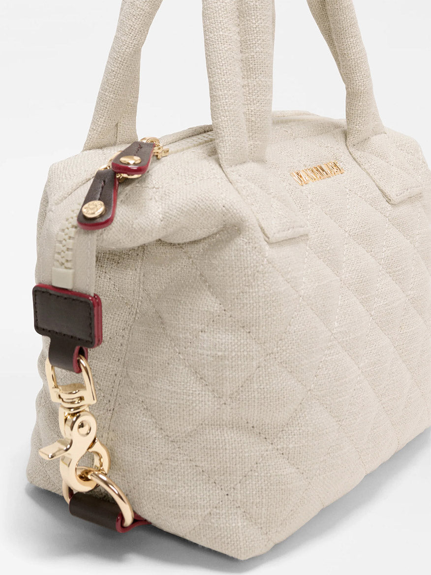 The MZ Wallace Micro Sutton in Sandy Linen Fabric is a beige quilted handbag with gold hardware, top handles, and a detachable strap with red and dark brown accents—a compact, stylish crossbody for any occasion.