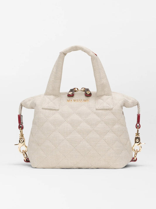 The MZ Wallace Micro Sutton in Sandy Linen Fabric is a small, quilted beige handbag with short handles, gold hardware, and red accents on the detachable shoulder strap attachments for a structured carry.
