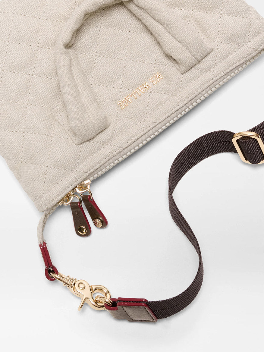 Close-up of a beige quilted bag with gold zippers, brown detachable strap with gold hardware, and elegant style—reminiscent of the MZ Wallace Micro Sutton in Sandy Linen Fabric.