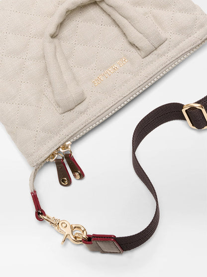 Close-up of a beige quilted bag with gold zippers, brown detachable strap with gold hardware, and elegant style—reminiscent of the MZ Wallace Micro Sutton in Sandy Linen Fabric.