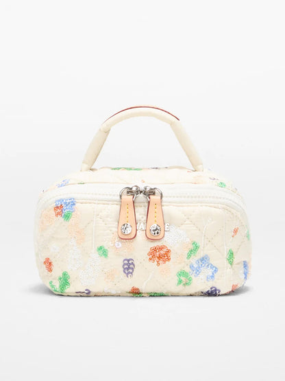 The MZ Wallace Mini Accordion Jewelry Case in Eden Sequin Oxford is a small, rectangular, cream-colored quilted bag with vibrant embroidery, a top handle, dual zippers, and multiple interior pockets for easy organization.