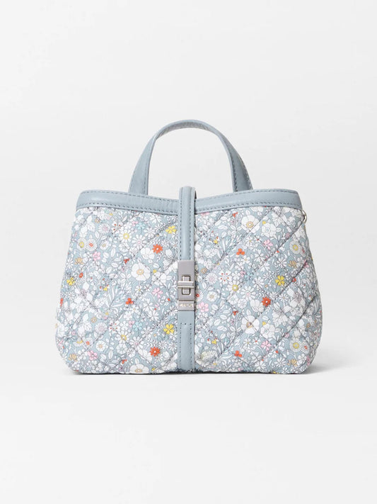 The MZ Wallace Mini Astor Top Handle in June's Meadow Liberty Fabric features a quilted light blue floral design, two short handles, and a silver clasp closure, displayed against a plain white background.