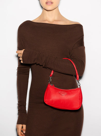 A person in a brown off-shoulder dress elegantly holds the MZ Wallace Mini Chelsea Shoulder in Bright Cherry Bedford against a plain background.