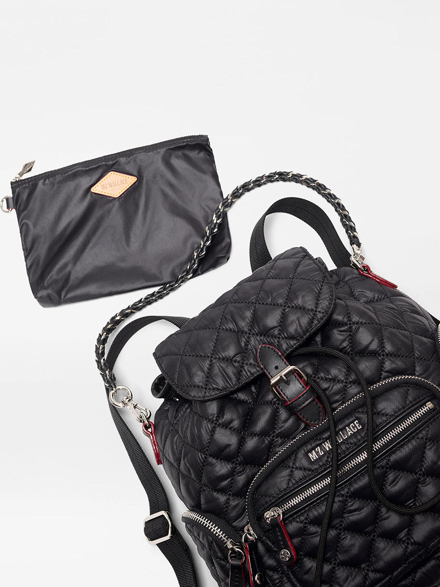 The MZ Wallace Mini Crosby Backpack in Black Oxford, featuring a quilted design, zippered pockets, and chain details, is displayed beside a matching black zip pouch against a plain background.
