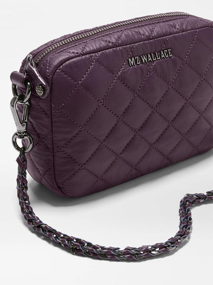 The MZ Wallace Mini Crosby Crossbody II in Raisin Oxford, shown on a white surface, features a quilted purple exterior crafted from recycled Oxford nylon. It is accented with a silver-tone zipper and a chain strap woven with purple material, and includes detachable straps for versatile styling.