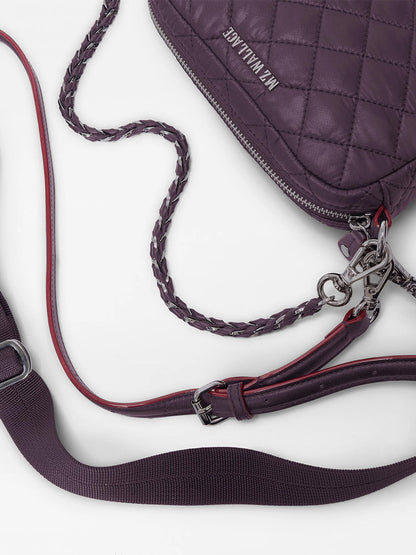 Close-up of the MZ Wallace Mini Crosby Crossbody II in Raisin Oxford—a quilted, purple handbag made from recycled Oxford nylon, featuring braided, adjustable detachable straps, metallic hardware, and “MM WILTWICE” text on the bag.