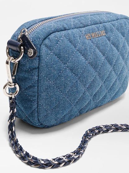 The MZ Wallace Mini Crosby Crossbody II in True Blue Denim is a quilted blue denim bag with a silver zipper, detachable chain strap, and front logo detailing.
