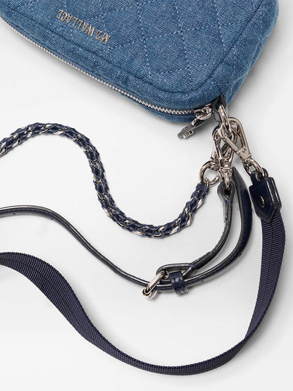 Close-up of the MZ Wallace Mini Crosby Crossbody II in True Blue Denim featuring a quilted design, metal zipper, detachable chain strap, leather accents, and metal hardware on a white background.