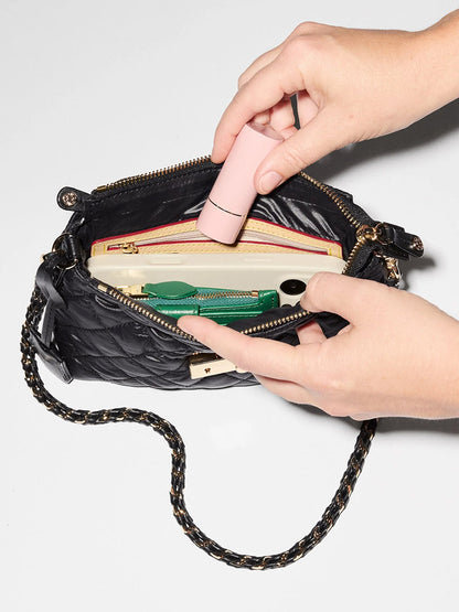 Hands place a small pink lipstick into a black quilted MZ Wallace Mini Crosby Lock Shoulder in Black Oxford containing a smartphone and a green wallet.