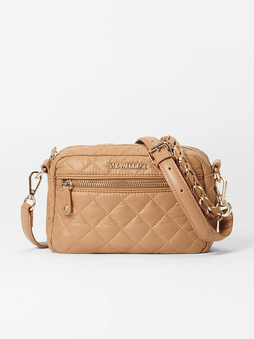 The MZ Wallace Mini Crosby in Caramel Oxford is a quilted crossbody bag made from luxurious Italian leather, featuring gold hardware, zipper pockets, and a detachable crossbody strap.