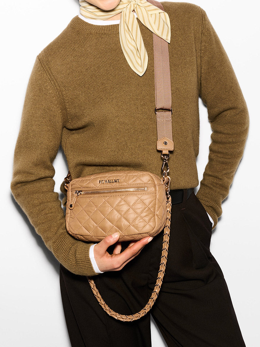 A person in a brown sweater, cream scarf, and black pants models an MZ Wallace Mini Crosby in Caramel Oxford, featuring a quilted design with a stylish Italian leather crossbody strap across their chest.