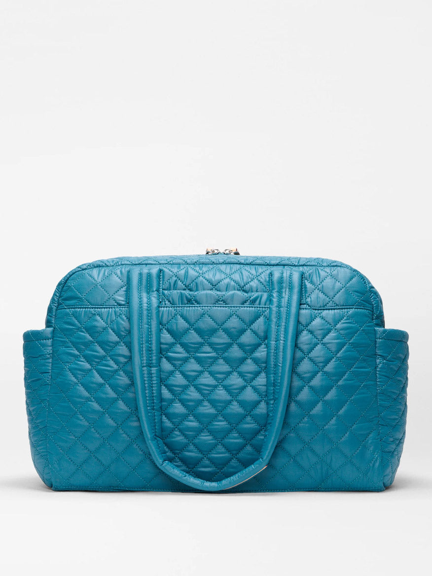 The MZ Wallace Nik Duffel in Pacific Oxford is a blue quilted handbag, crafted as a chic travel carryall—perfect for stylish journeys.