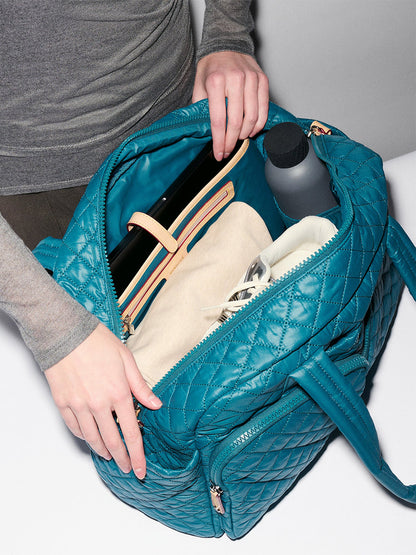 Someone opens the MZ Wallace Nik Duffel in Pacific Oxford to reveal a beige pouch, a water bottle, and a laptop inside.