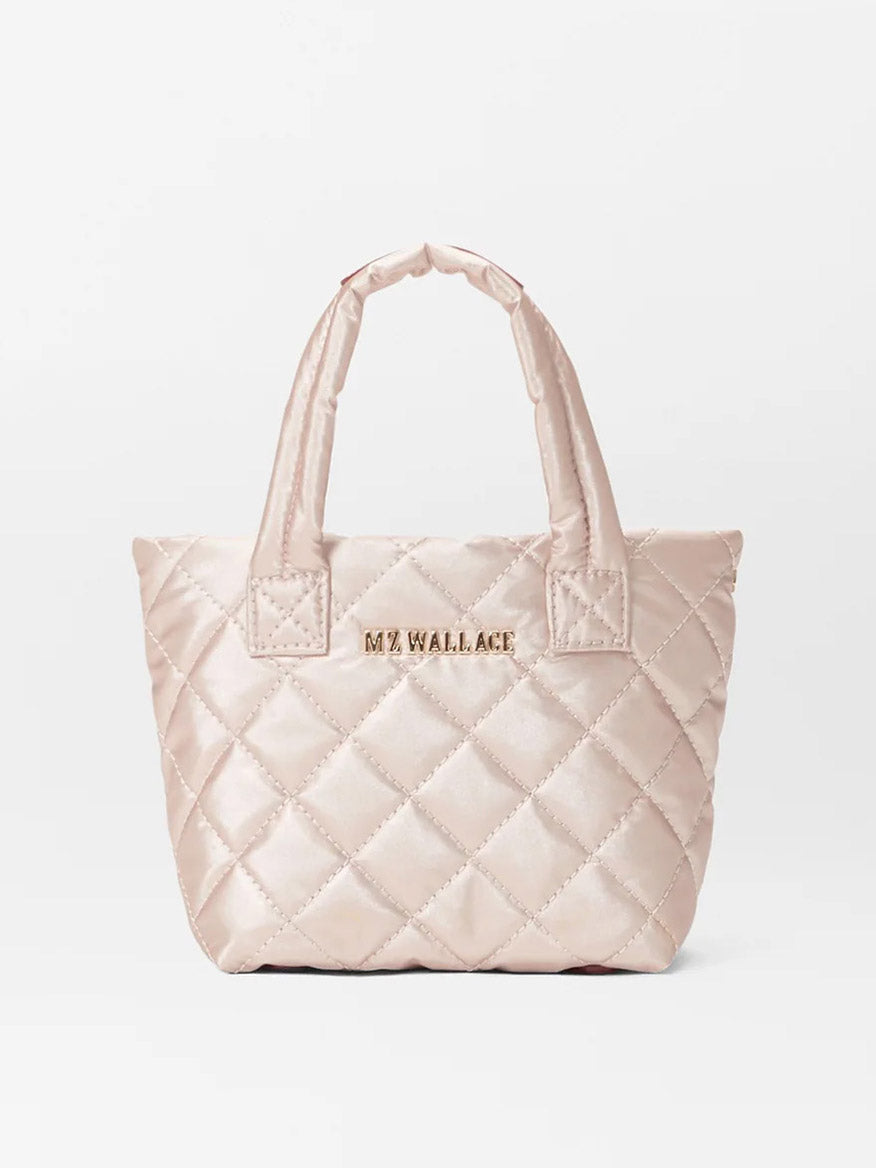 A quilted handbag in a pale rose gold metallic Oxford finish from MZ Wallace, featuring foldable design and "MZ WALLACE" in gold lettering on the front, along with a crossbody strap for versatile carrying options.