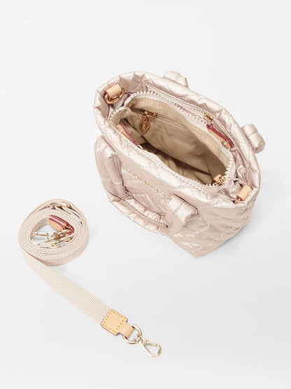 The MZ Wallace Petite Metro Tote Deluxe in Pale Rose Gold Metallic Oxford features an open top view, showcasing a beige interior. It is adorned with gold zippers and comes with a detachable crossbody strap placed on the side.