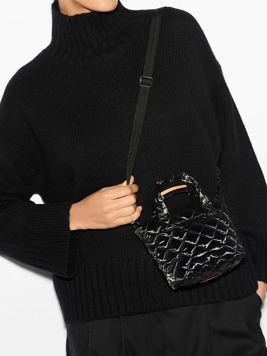 A person wearing a black turtleneck sweater is holding a chic quilted mini nylon bag from the MZ Wallace Petite Metro Tote Deluxe collection in Black Liquid Oxford.