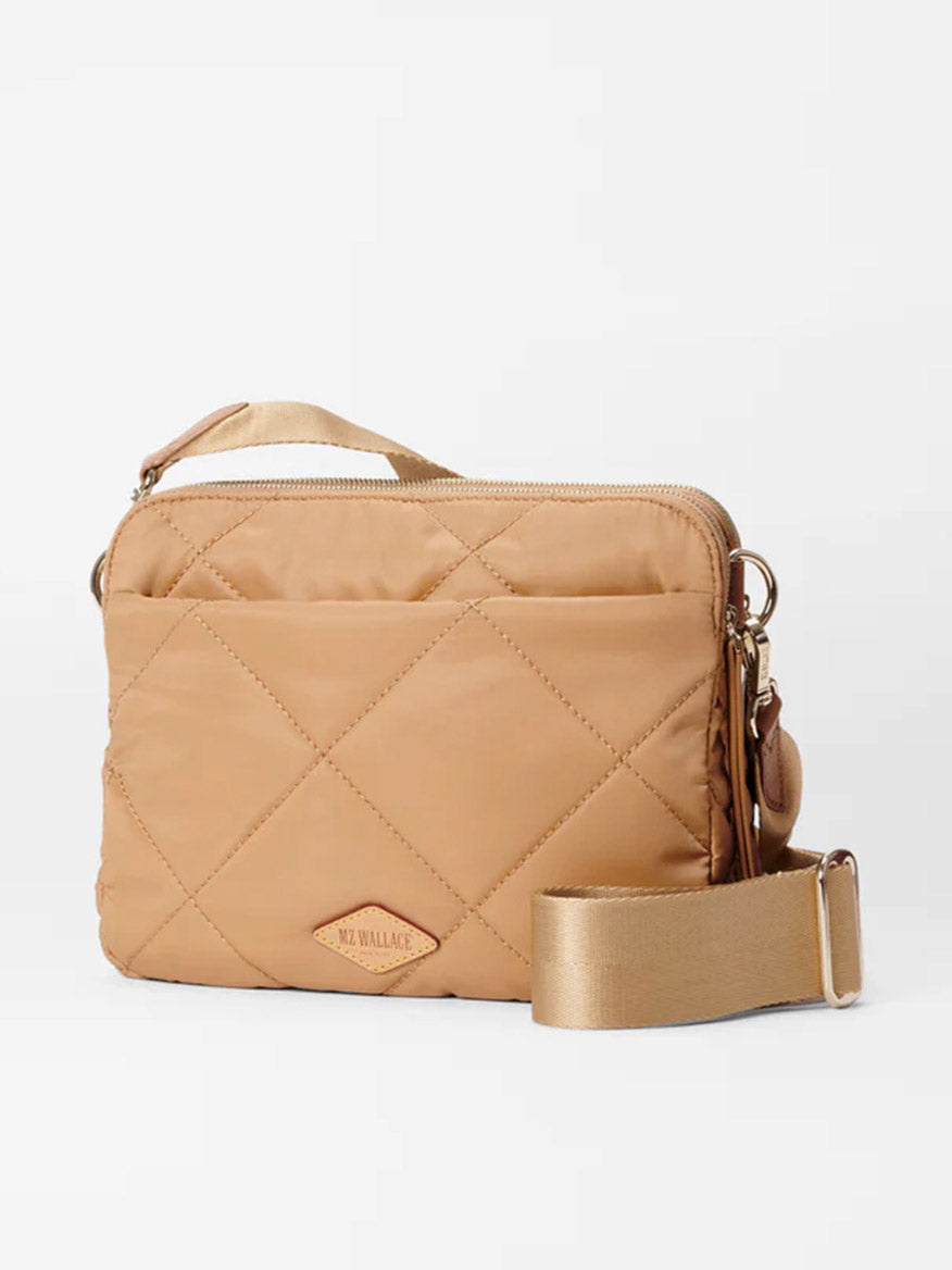 The MZ Wallace Quilted Madison Crossbody in Caramel Bedford is a tan bag made from recycled nylon with Italian leather trim, featuring a detachable strap, zipper closure, and a chic logo tag on the front.