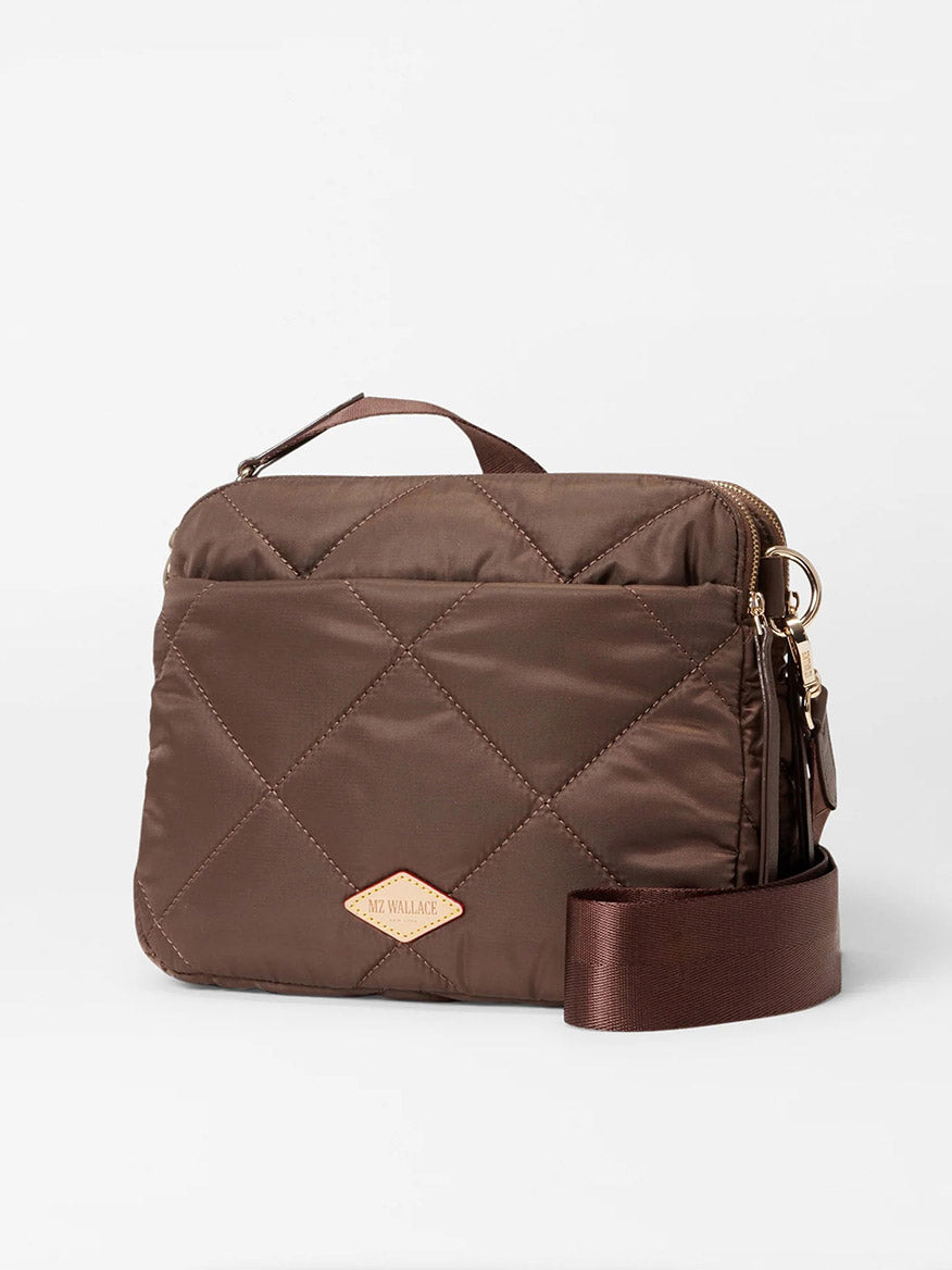 The MZ Wallace Quilted Madison Crossbody in Walnut Bedford, made from recycled nylon, showcases a brown quilted design with a top handle, gold zipper, and adjustable strap against a white background.