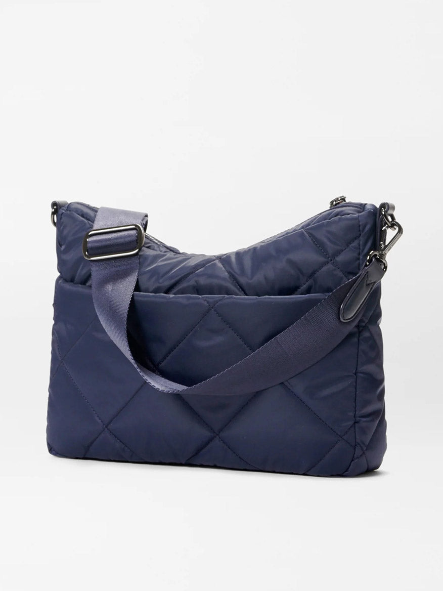 The MZ Wallace Quilted Madison Uptown Crossbody in Dawn is a quilted navy blue shoulder bag featuring adjustable straps, Italian leather detailing, metal clasps, and a zippered top closure against a plain white background.