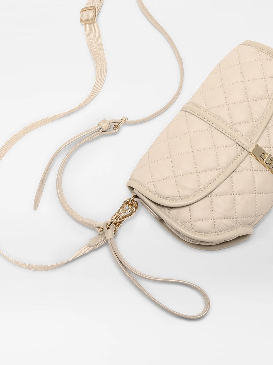 The MZ Wallace Small Astor Convertible Clutch in Buff Oxford features quilted beige nylon, gold hardware, and an adjustable Italian leather strap, shown on a white background.