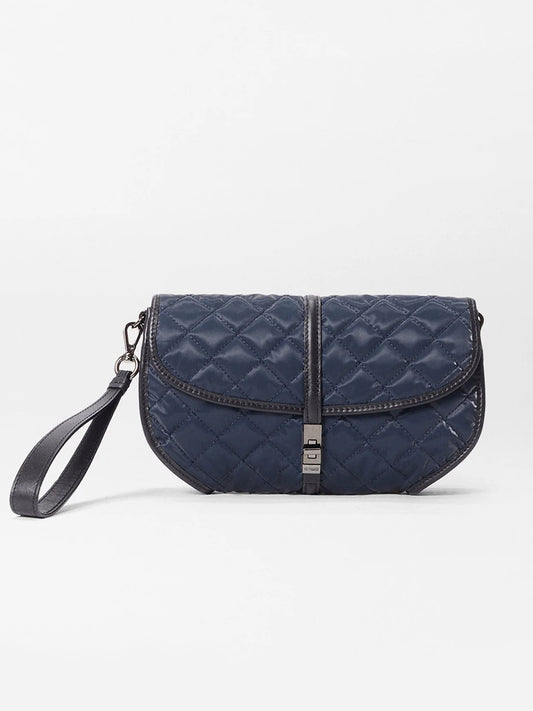 The MZ Wallace Small Astor Convertible Clutch in Ink Liquid Oxford features a navy blue quilted design, black wrist strap, front flap, and buckle closure, displayed on a plain white background.