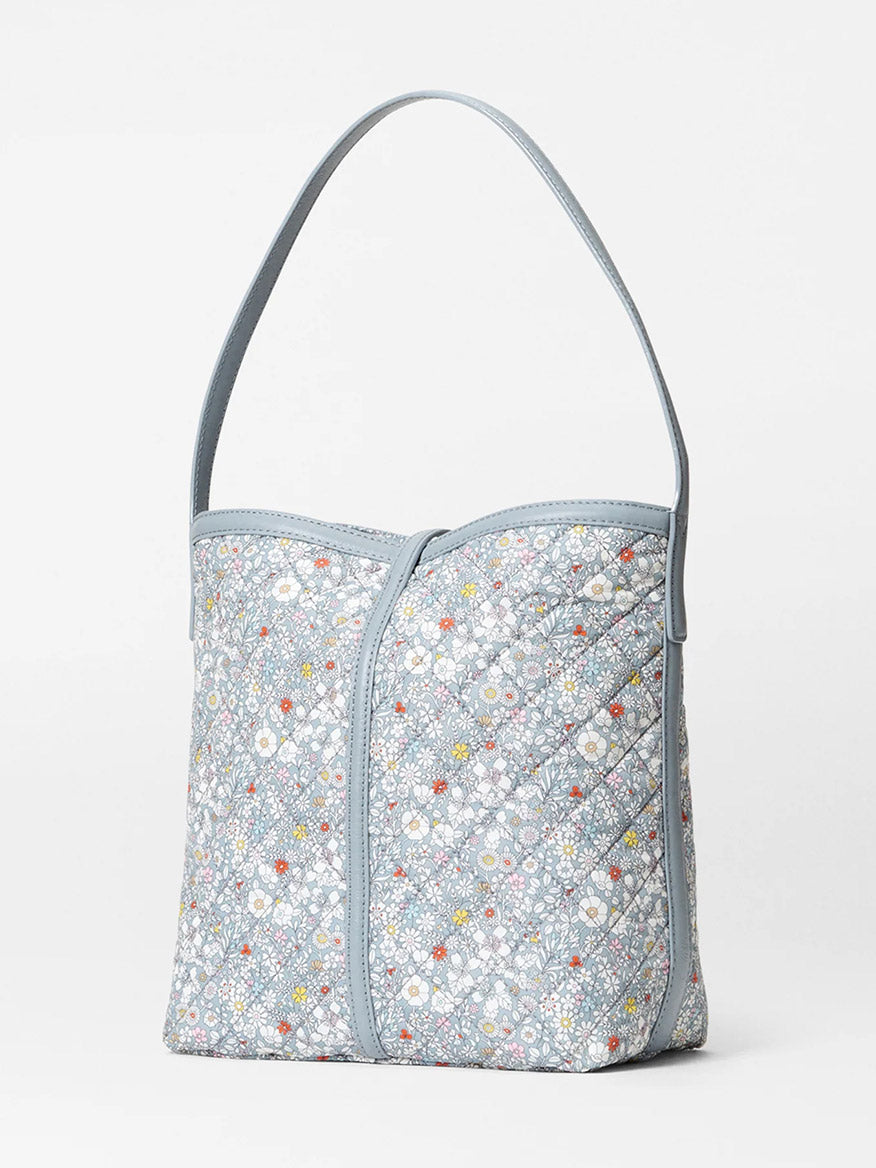The MZ Wallace Small Astor Hobo in June's Meadow Liberty Fabric features light blue quilted nylon with a floral pattern, zip closure, and single strap. Displayed against a plain white background.