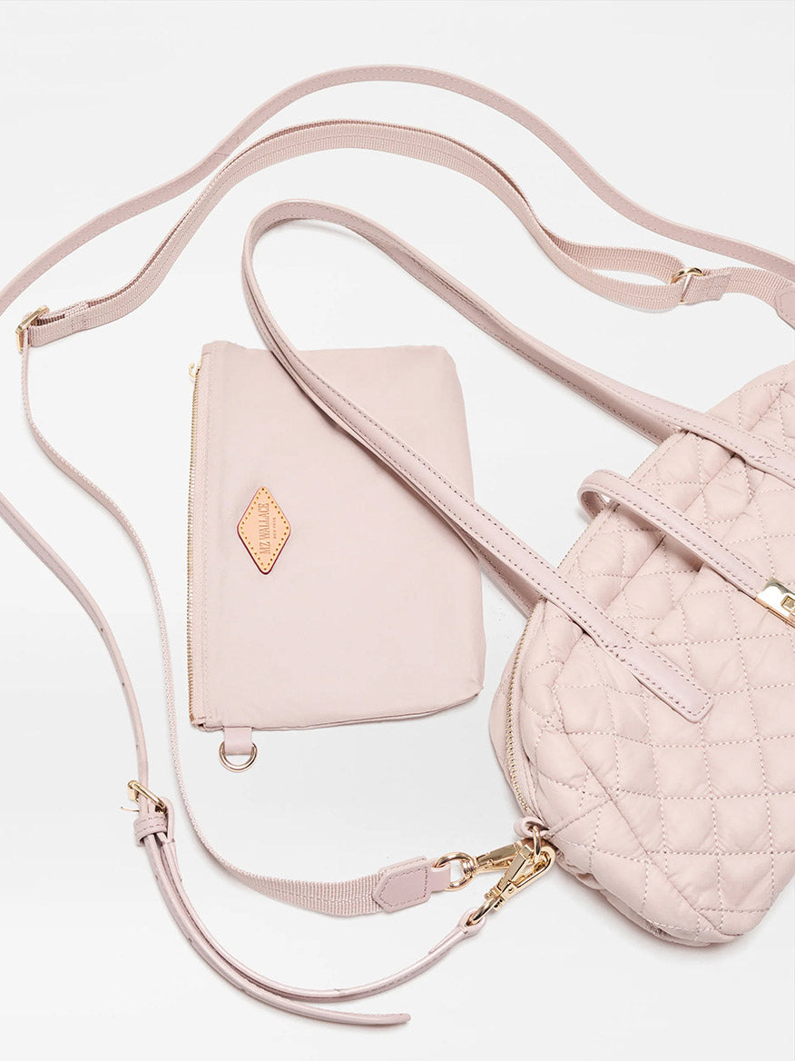 The MZ Wallace Small Astor Satchel in City Pink Oxford, featuring a light pink quilted nylon body with Italian leather trim and gold hardware, is paired with a matching zippered pouch and displayed against a white background.