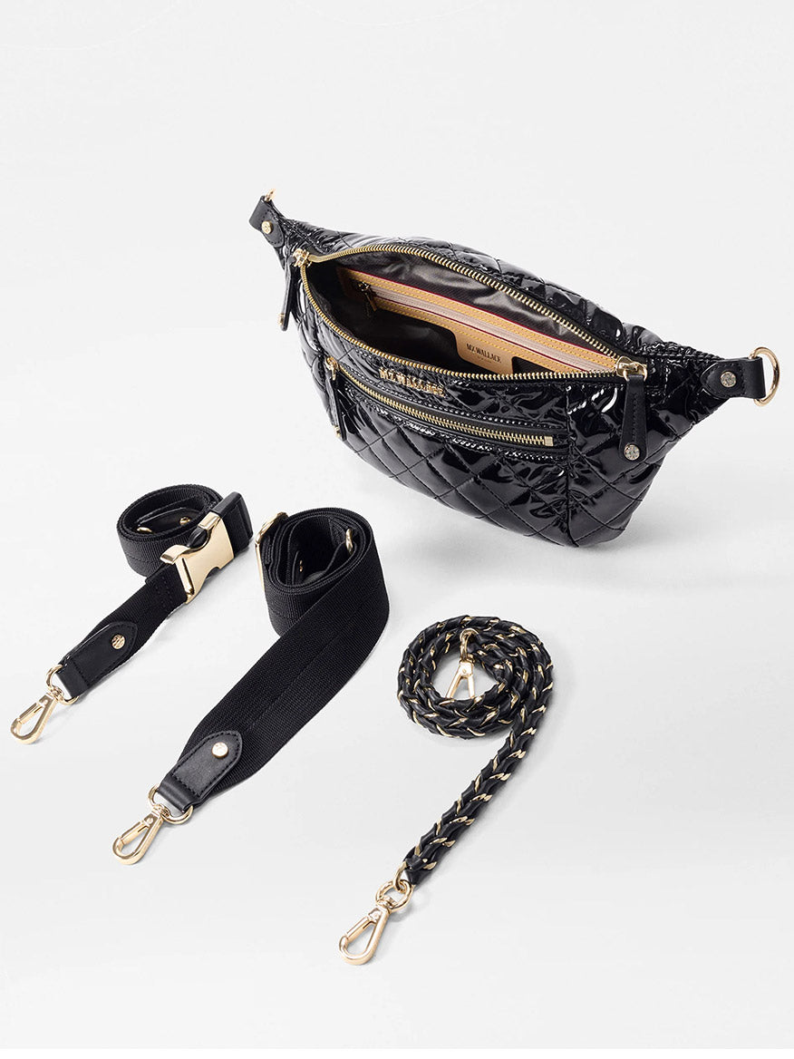 The MZ Wallace Small Crosby Sling Bag in Black Lacquer Oxford is a sleek quilted crossbody featuring gold zippers, two detachable black straps, and a braided strap, elegantly displayed on a white surface.