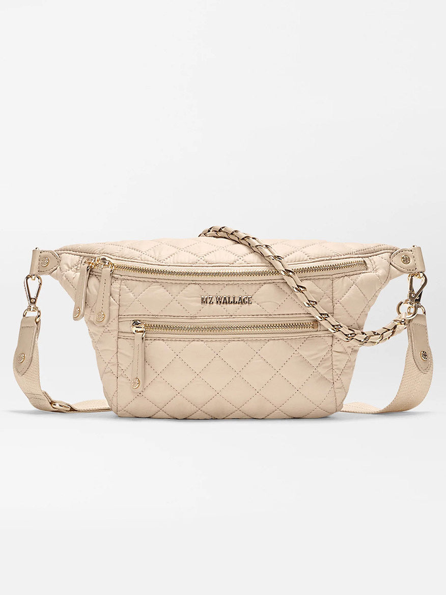 The MZ Wallace Small Crosby Sling Bag in Buff Oxford is a beige quilted crossbody featuring gold zippers, front pockets, and an adjustable strap with chain accents.
