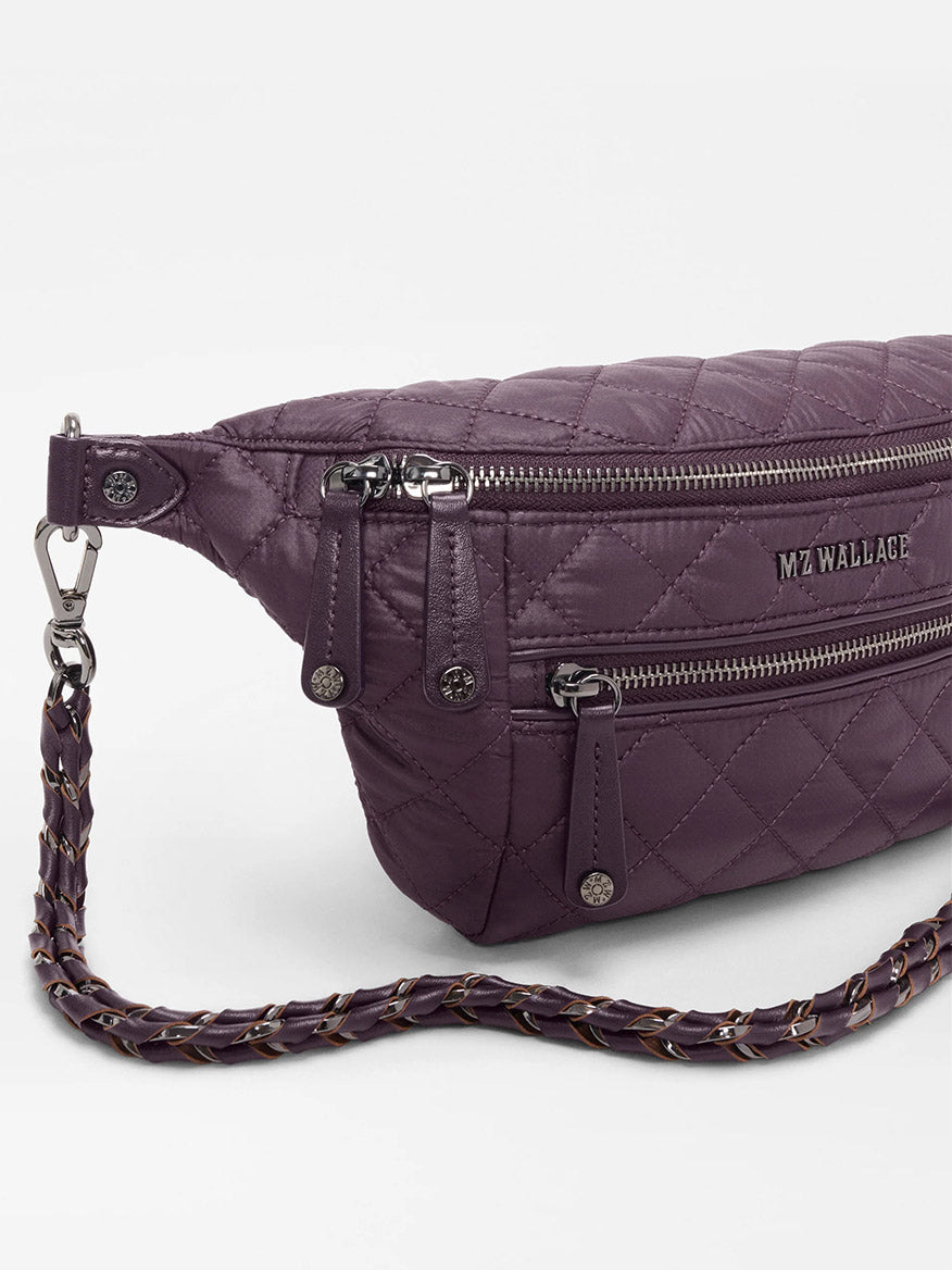 The MZ Wallace Small Crosby Sling Bag in Raisin Oxford features a quilted design, two zippered compartments, and a woven adjustable strap, shown against a white background.