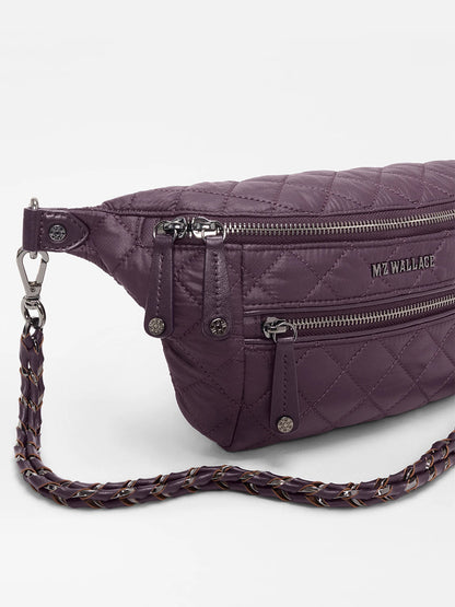 The MZ Wallace Small Crosby Sling Bag in Raisin Oxford features a quilted design, two zippered compartments, and a woven adjustable strap, shown against a white background.