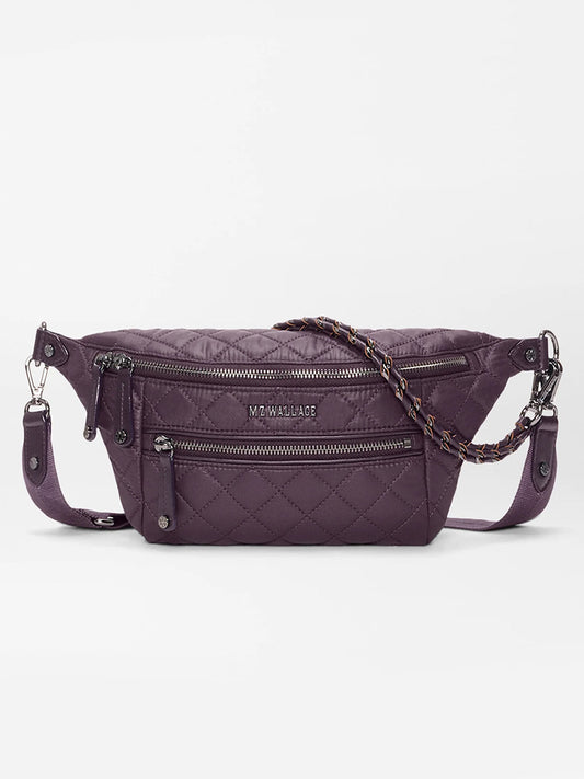 The MZ Wallace Small Crosby Sling Bag in Raisin Oxford features quilted purple fabric, two front zip pockets, a chain-accented shoulder strap, and the MZ WALLACE logo on the front.