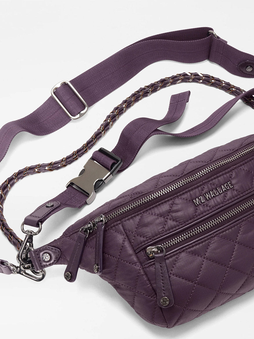 The MZ Wallace Small Crosby Sling Bag in Raisin Oxford features silver zippers, an adjustable strap, and a chain accent detail, shown on a white background.