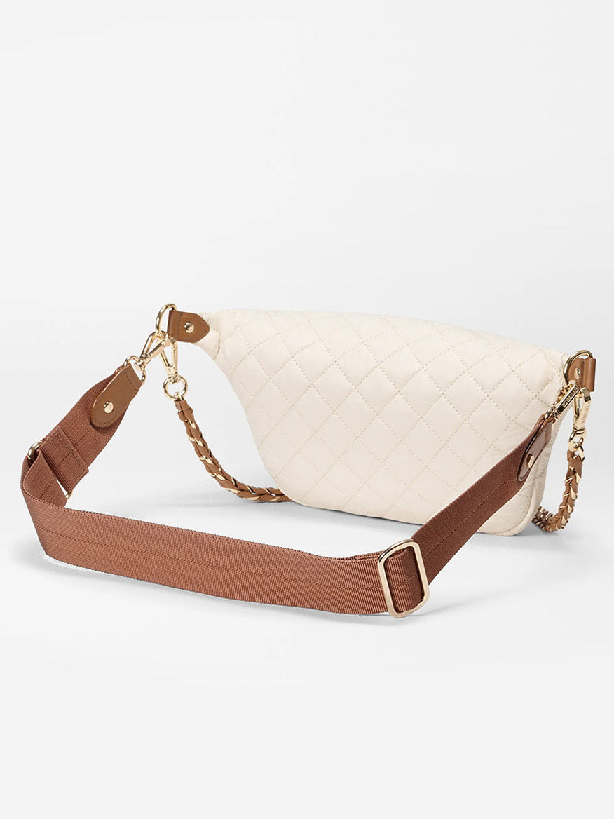 The MZ Wallace Small Crosby Sling Bag in Sandshell Oxford With Brown, featuring gold hardware, a quilted cream design, wide brown adjustable strap, and exterior pockets, is shown against a plain white background.