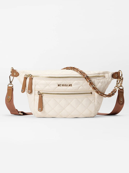 The MZ Wallace Small Crosby Sling Bag in Sandshell Oxford with Brown features quilted cream fabric, gold zippers, brown leather accents, an adjustable strap, and a braided handle, shown on a white background.