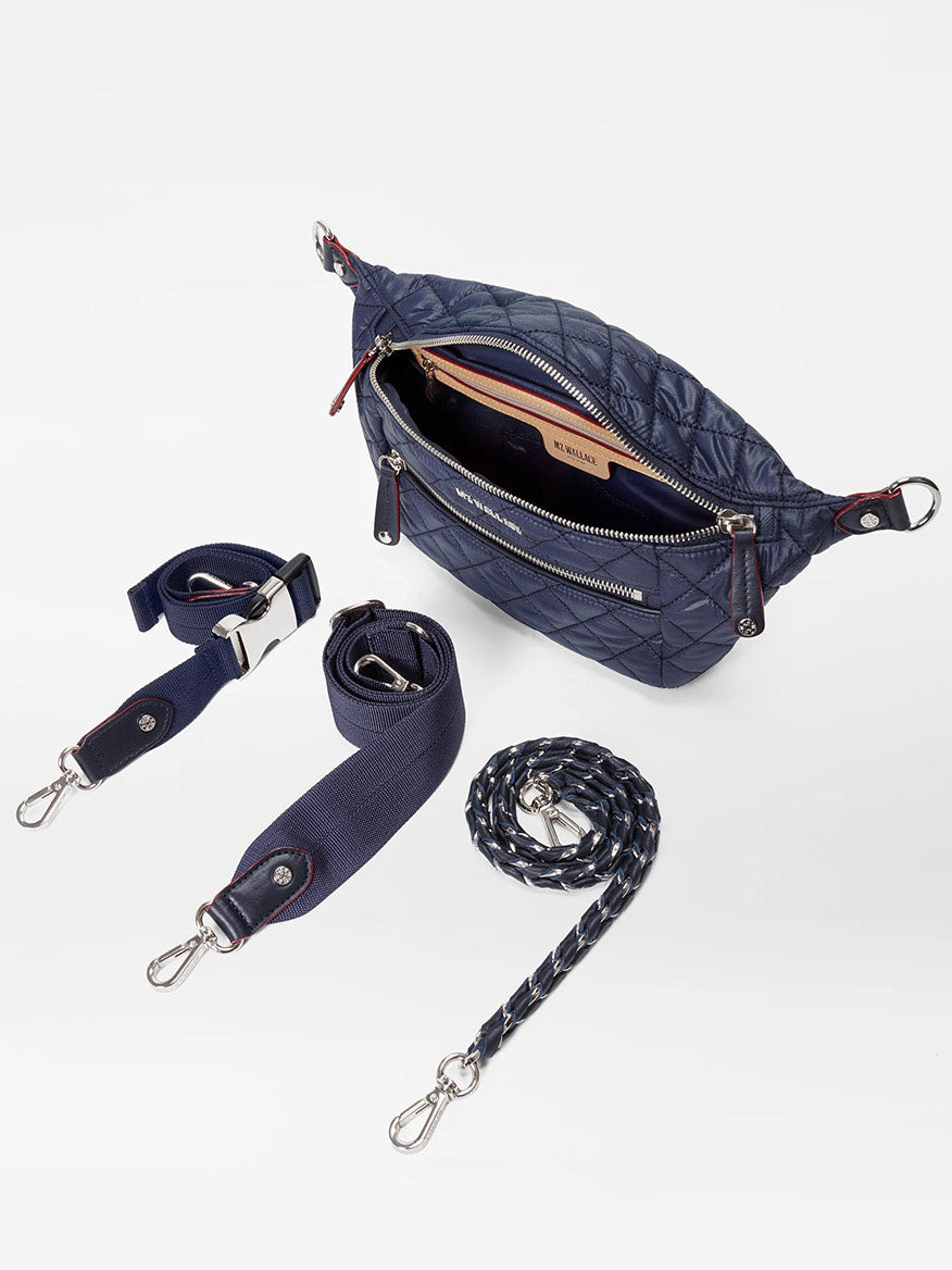 The MZ Wallace Small Crosby Sling Bag in Dawn Oxford is a navy quilted crossbody with an open zipper, three detachable straps (including one braided), and silver hardware, displayed on a white background.