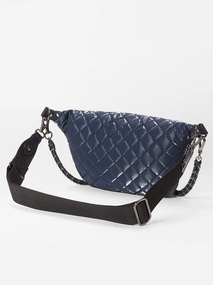 The MZ Wallace Small Crosby Sling Bag in Ink Liquid Oxford features a glossy navy blue quilted finish and an adjustable black shoulder strap, shown against a white background.