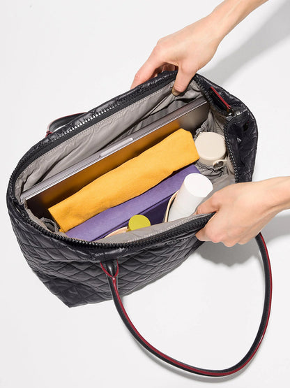 Top view of an open MZ Wallace Small Daily Tote in Black Oxford holding a laptop, yellow and purple pouches, a notebook, and several bottles.